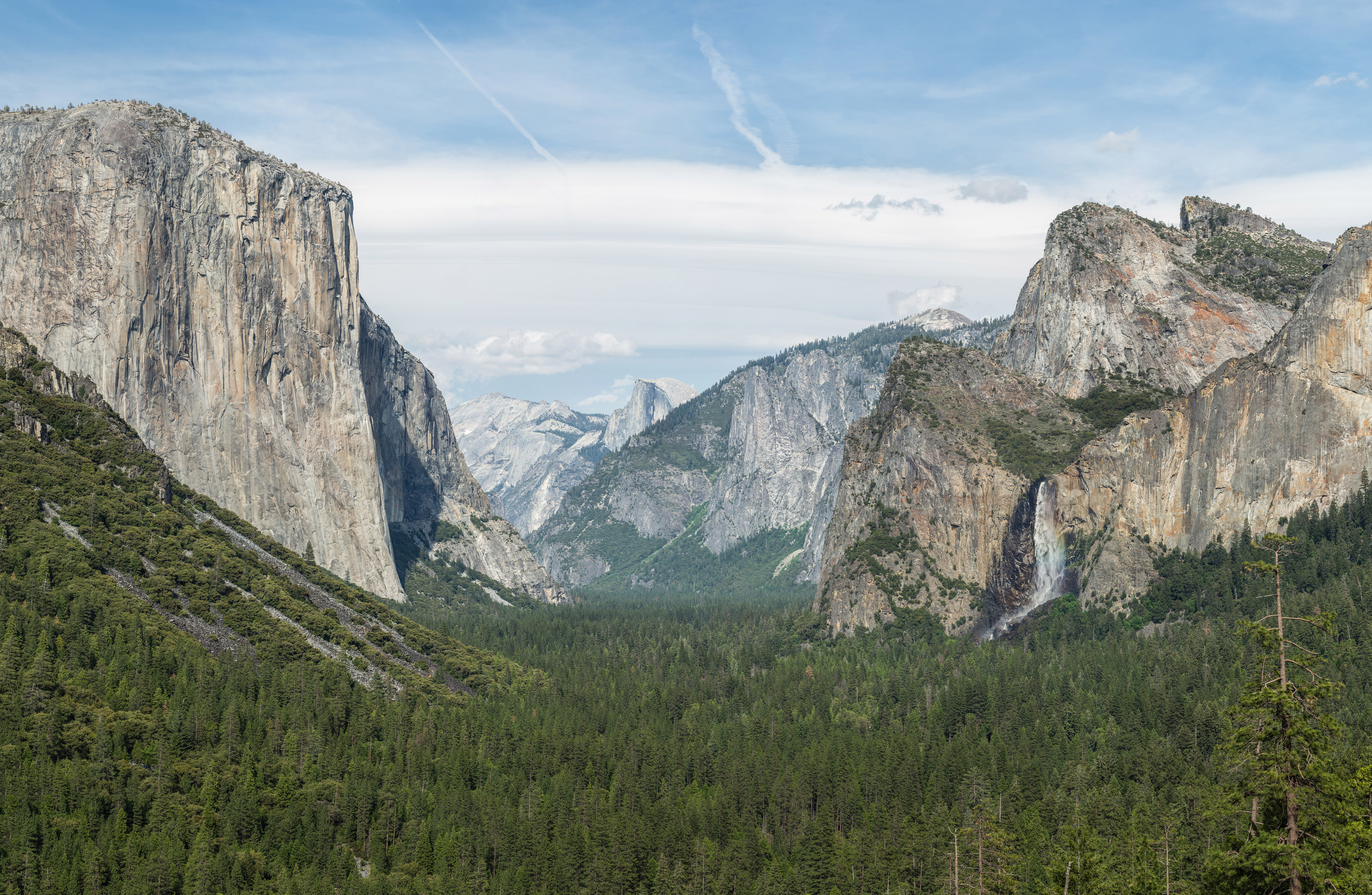 A wide scenic photograph from Tunnel View looking into Yosemite Valley with El Capitan on the left, Bridalveil Fall on the right, and Half Dome in the distance under clear morning light