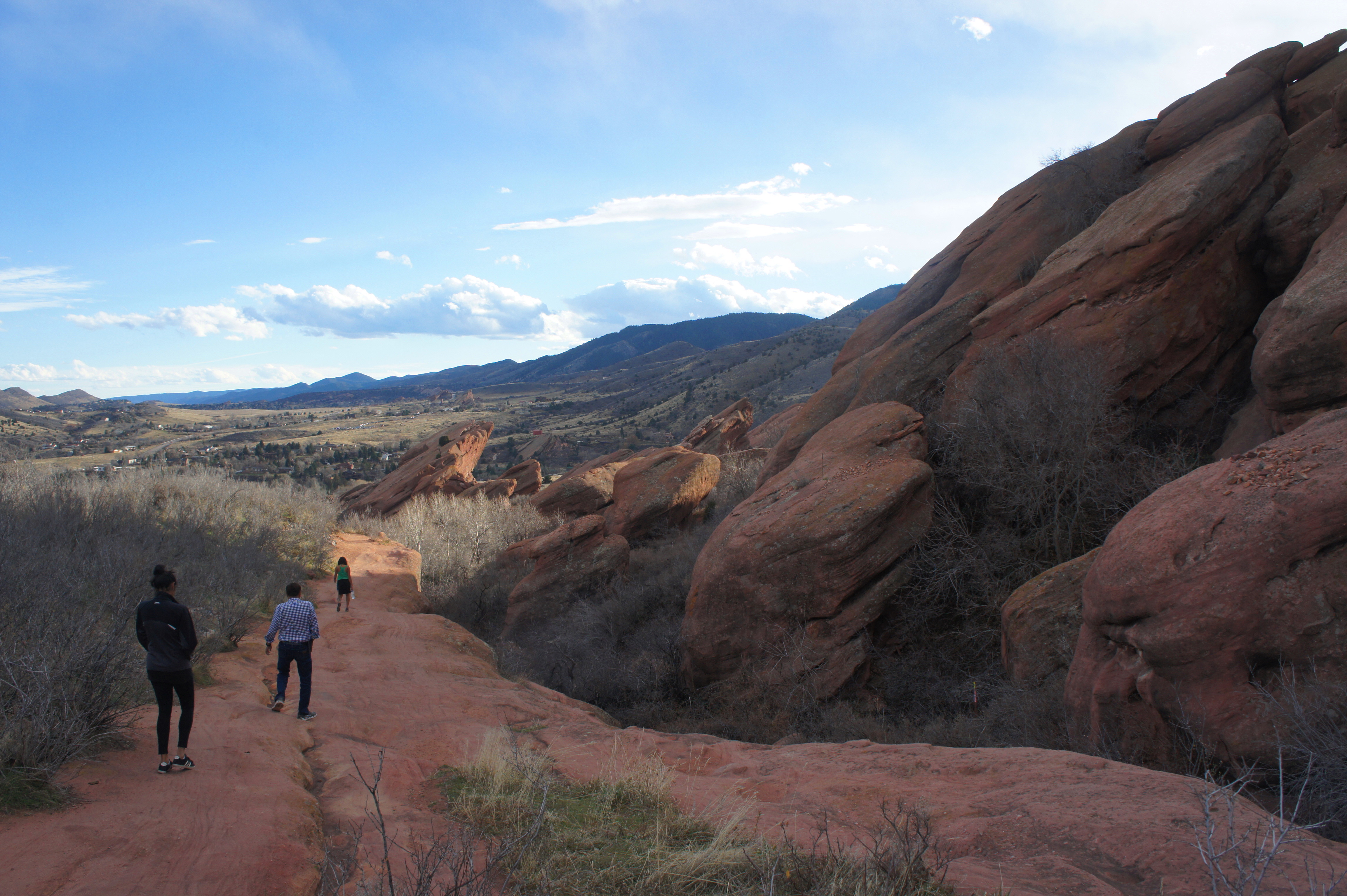 A winding hiking path through towering red sandstone formations at Red Rocks near Morrison, Colorado with hikers in the distance, warm morning light, photorealistic travel photography