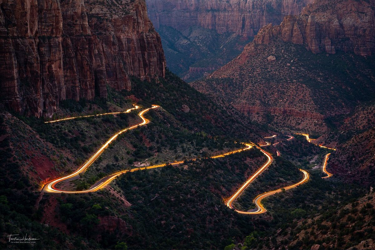 A winding section of Zion Mount Carmel Highway near the Zion tunnel with sandstone cliffs and a few cars navigating the curves in bright afternoon light, realistic travel photo