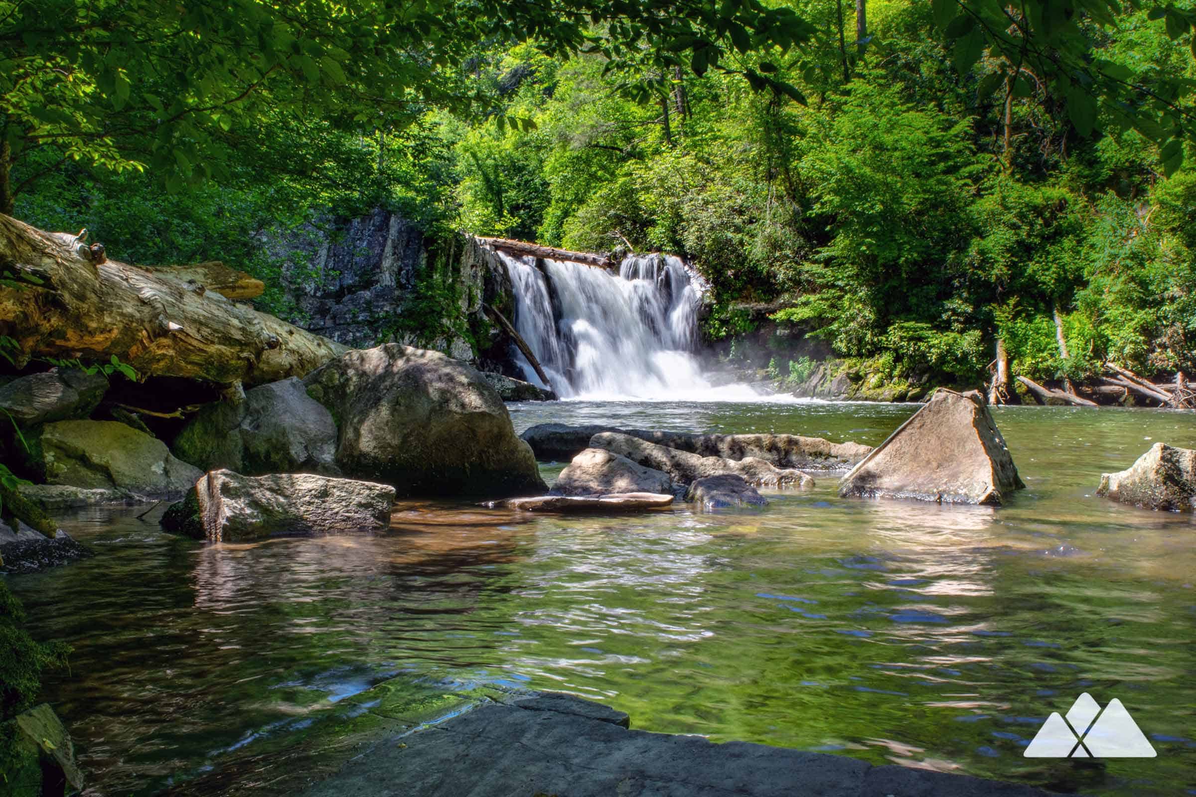 Abrams Falls wide waterfall pouring into a deep pool with hikers sitting on sunlit rocks along the shore, real photograph