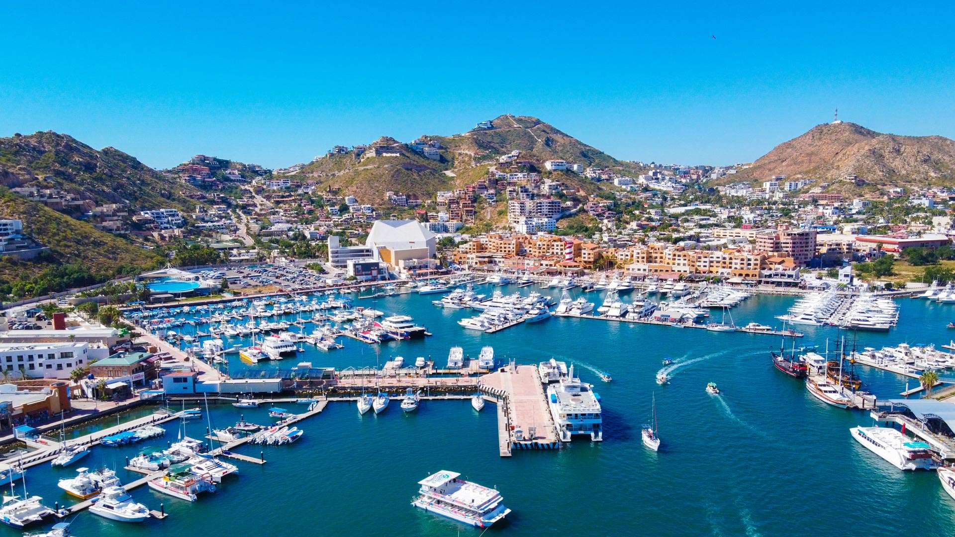 Cabo San Lucas marina at golden hour with docked boats, warm sunset light, and rocky headlands in the distance