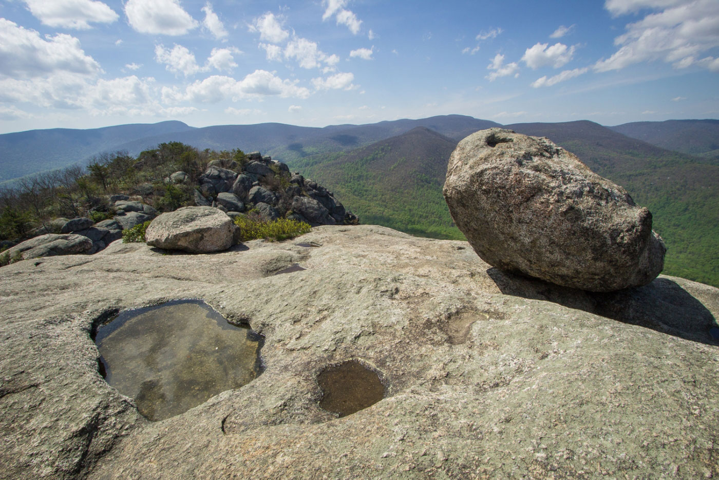 Close-up of sunlit granite boulders on Old Rag Mountain with a narrow scramble corridor and hikers carefully stepping through, realistic outdoor photography