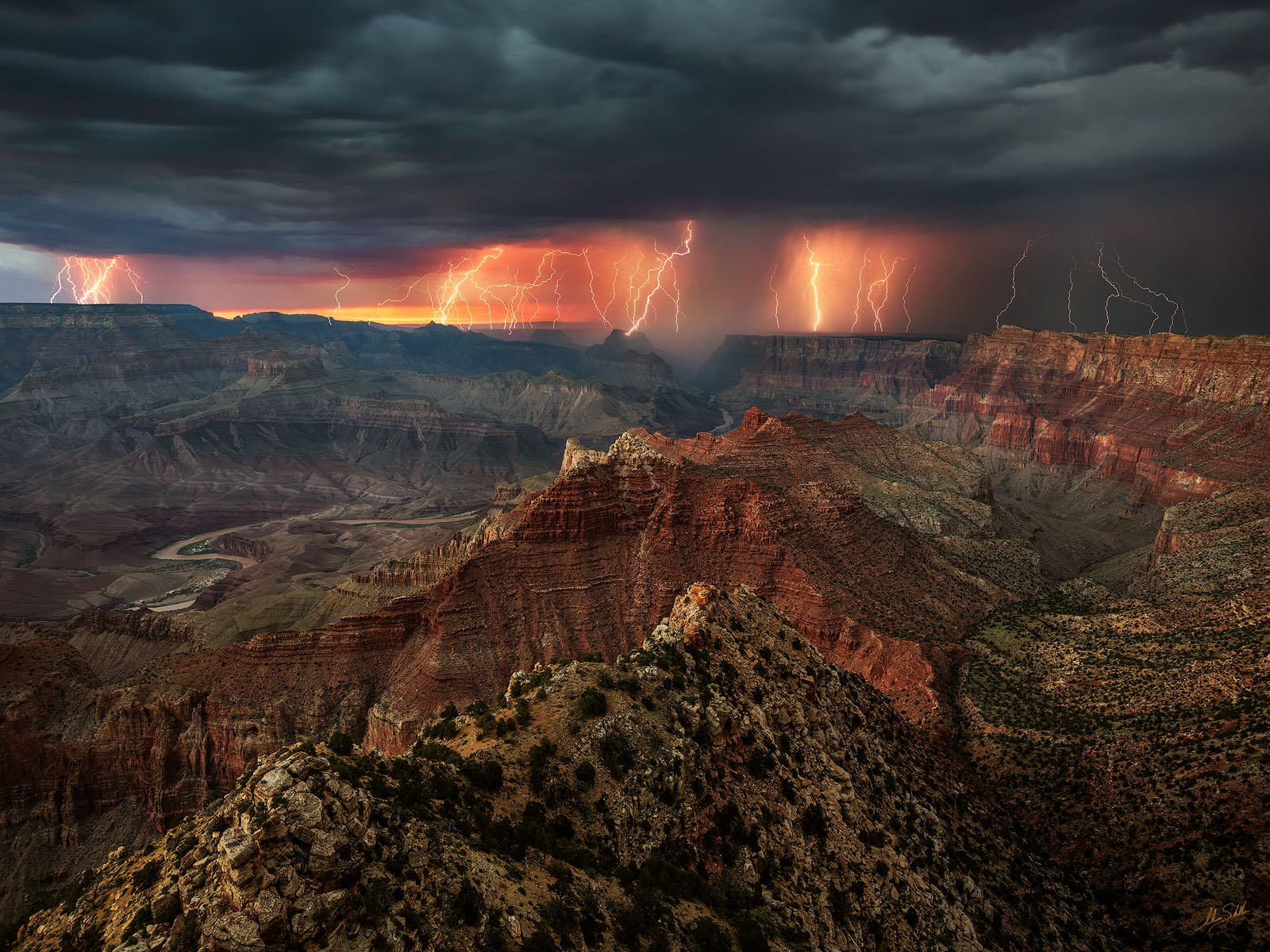 Dark monsoon storm clouds building over the Grand Canyon seen from the South Rim with sunlit canyon layers in the foreground, realistic photography