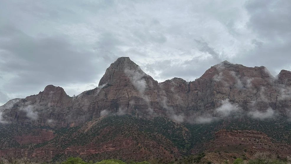 Dark storm clouds building above a narrow sandstone canyon in Zion National Park with a dry sandy wash below, dramatic weather photo