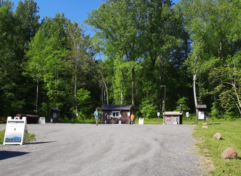Early morning at the Old Rag parking area near Nethers, Virginia, with a few parked cars, trailhead kiosk, and forest edge under soft sunrise light, realistic photography
