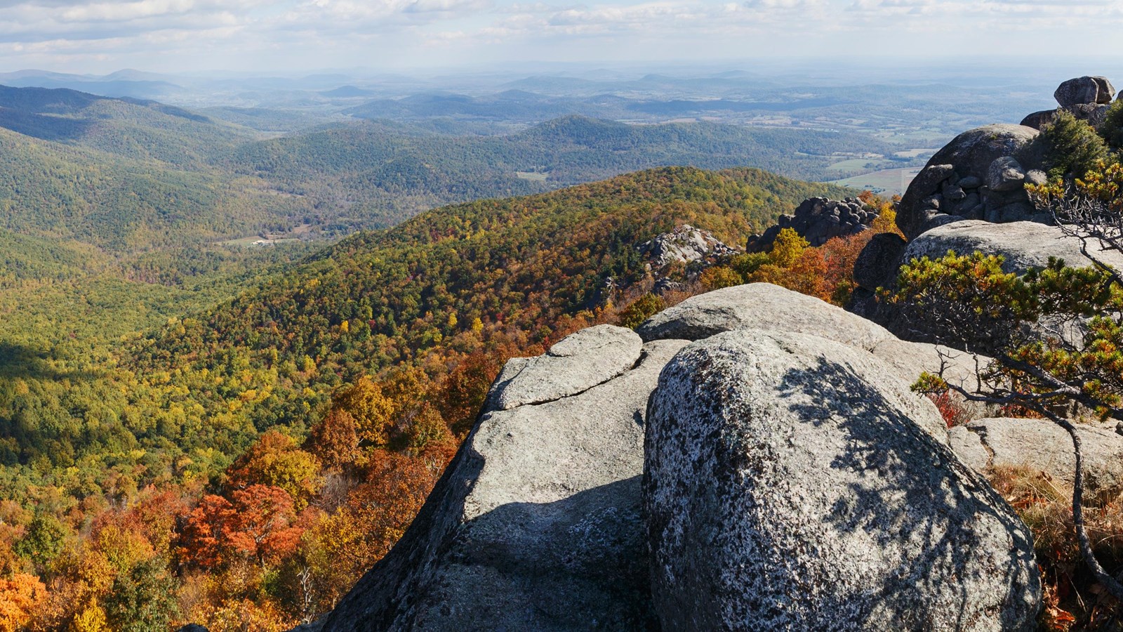 Hikers moving through the Old Rag Mountain rock scramble in Shenandoah National Park, hands on granite boulders with forested slopes in the background, realistic outdoor photography