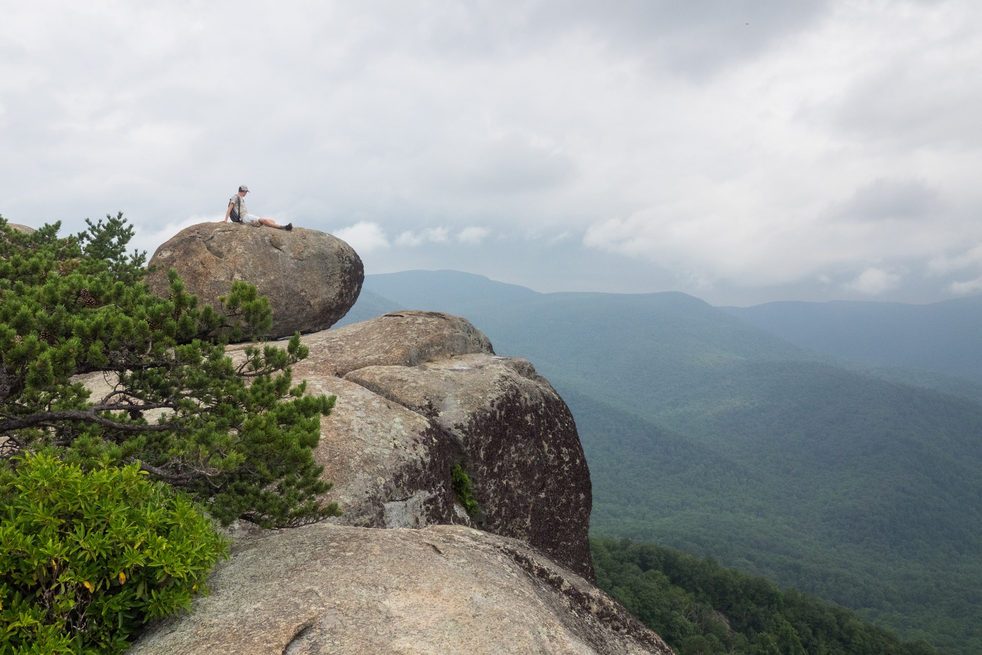 Hikers sitting on sunlit granite at the Old Rag Mountain summit in Shenandoah National Park, looking out over layered blue ridgelines, realistic outdoor photography