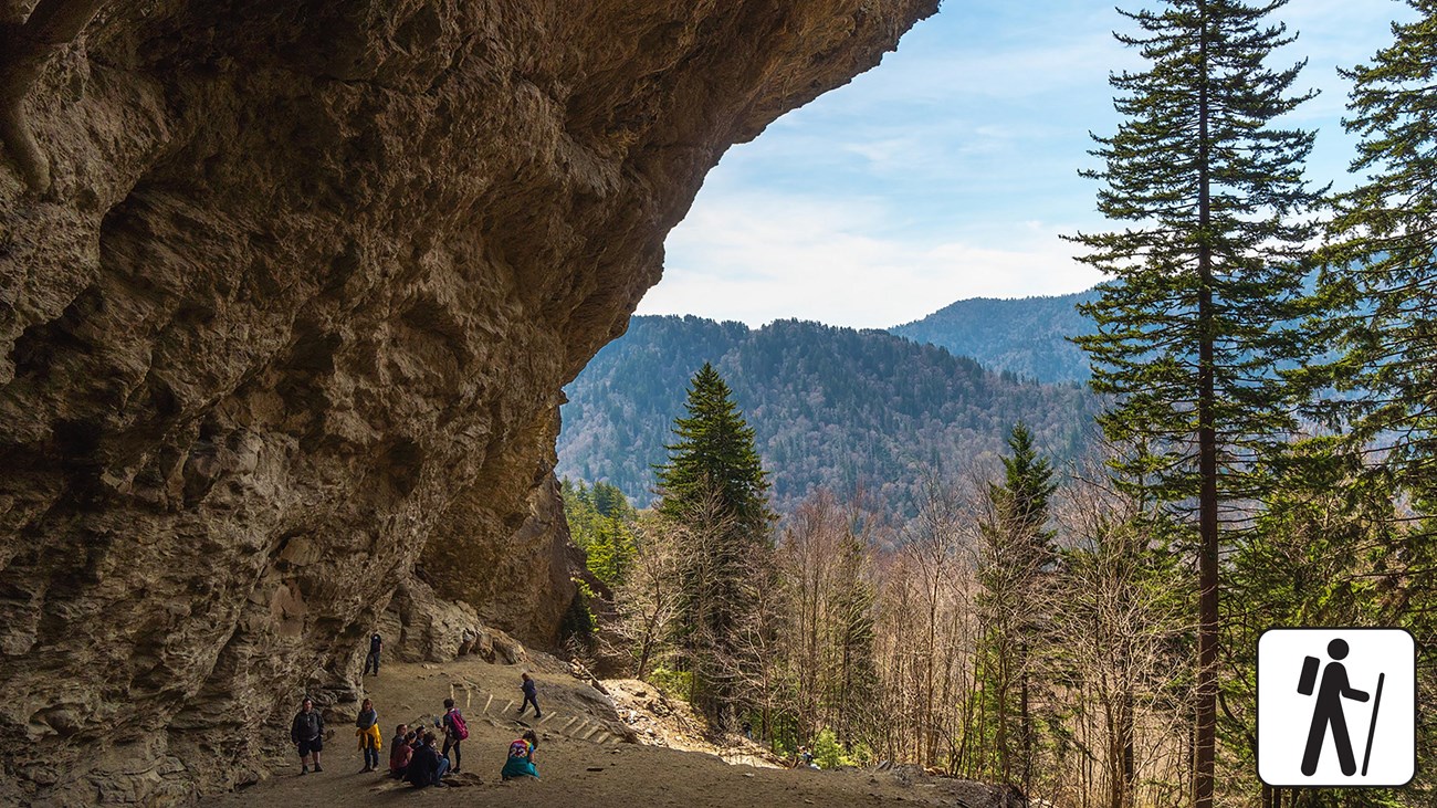 Hikers walking beneath the rocky overhang at Alum Cave Bluffs in Great Smoky Mountains National Park, textured stone ceiling and forested slope below, real outdoor photograph