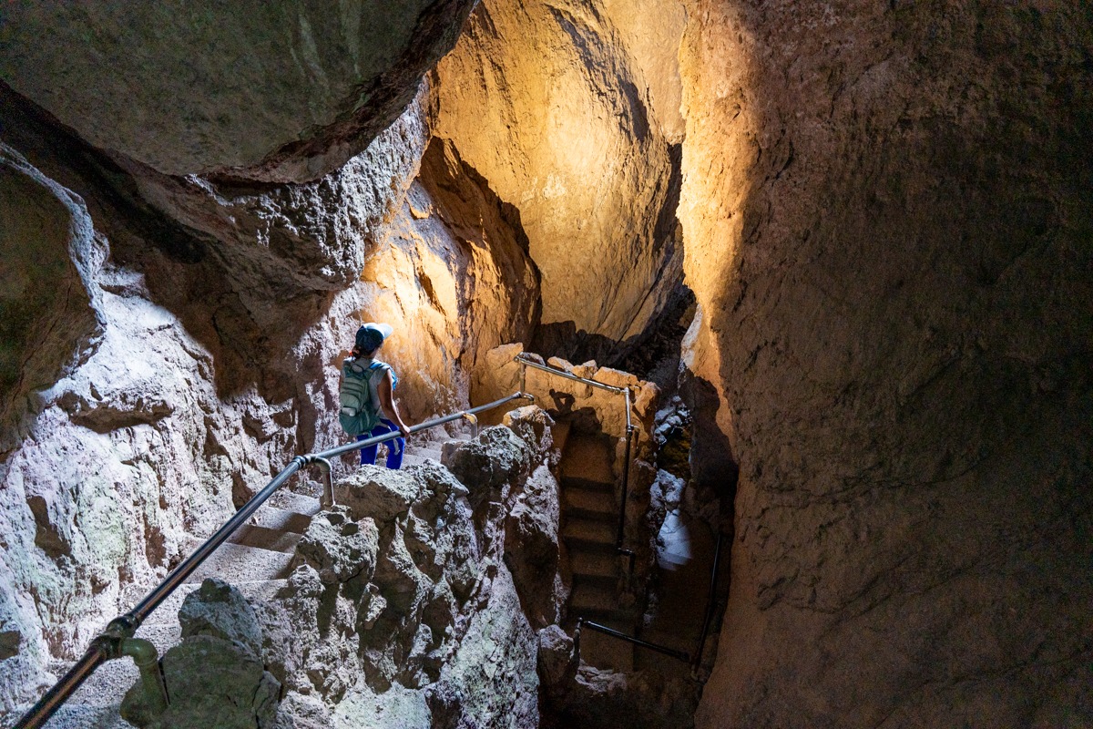 Hikers walking through the rocky Bear Gulch Cave at Pinnacles National Park with headlamps reflecting off boulders and uneven stone floor, realistic low-light photography