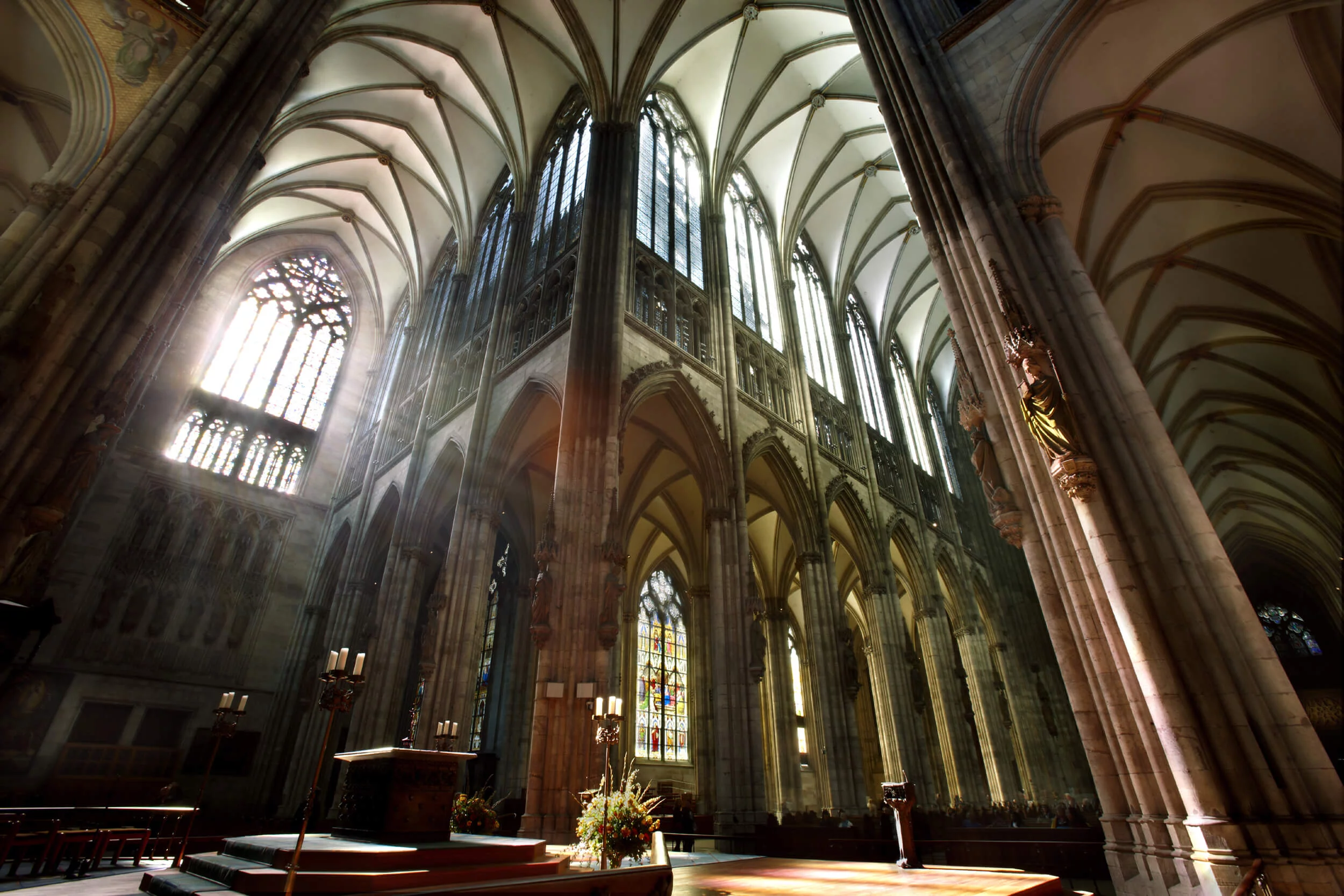 Inside Cologne Cathedral, the soaring nave with tall Gothic columns and stained-glass light falling across the stone floor