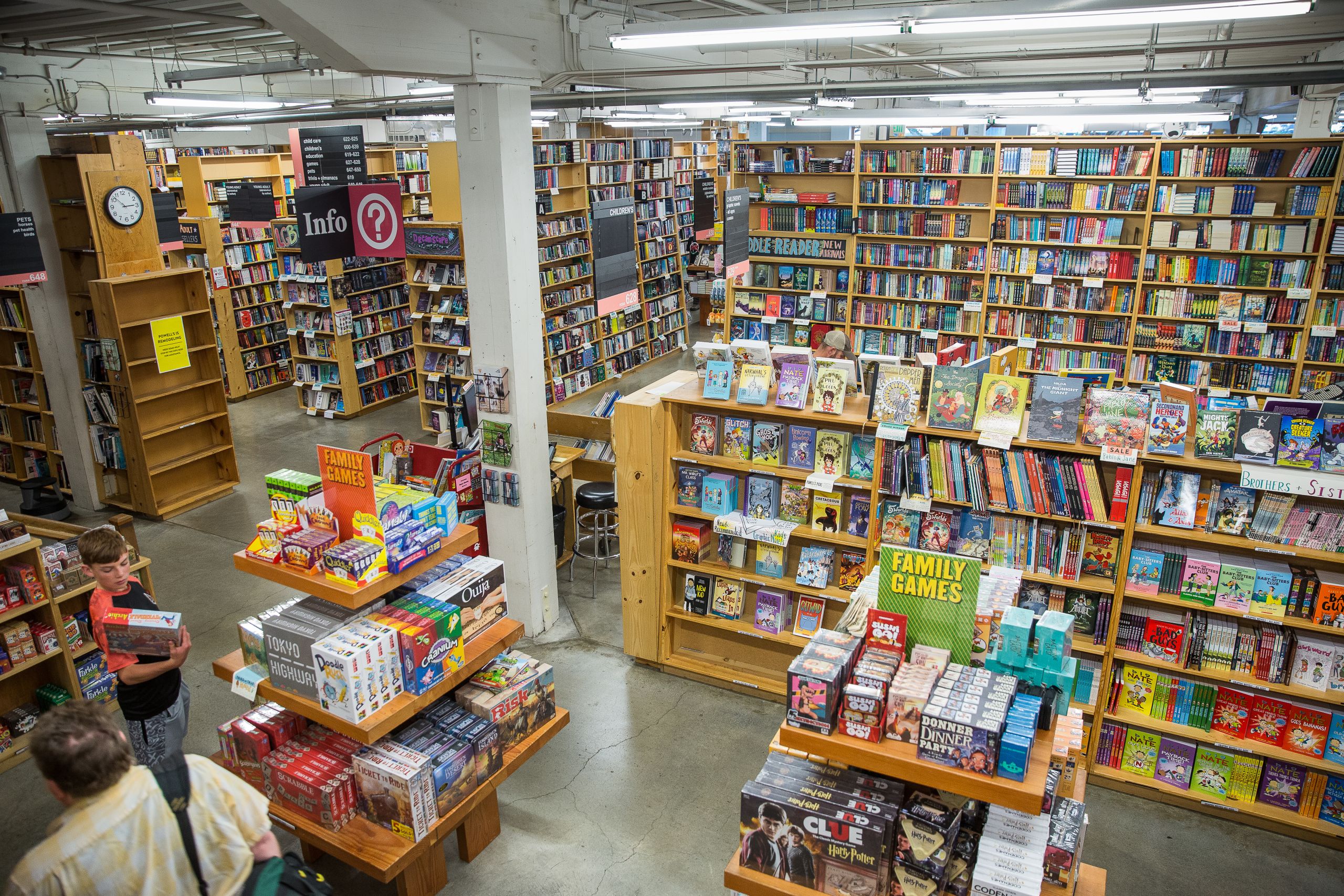 Inside Powell's City of Books with tall shelves, colorful section signs, and shoppers browsing in warm indoor light