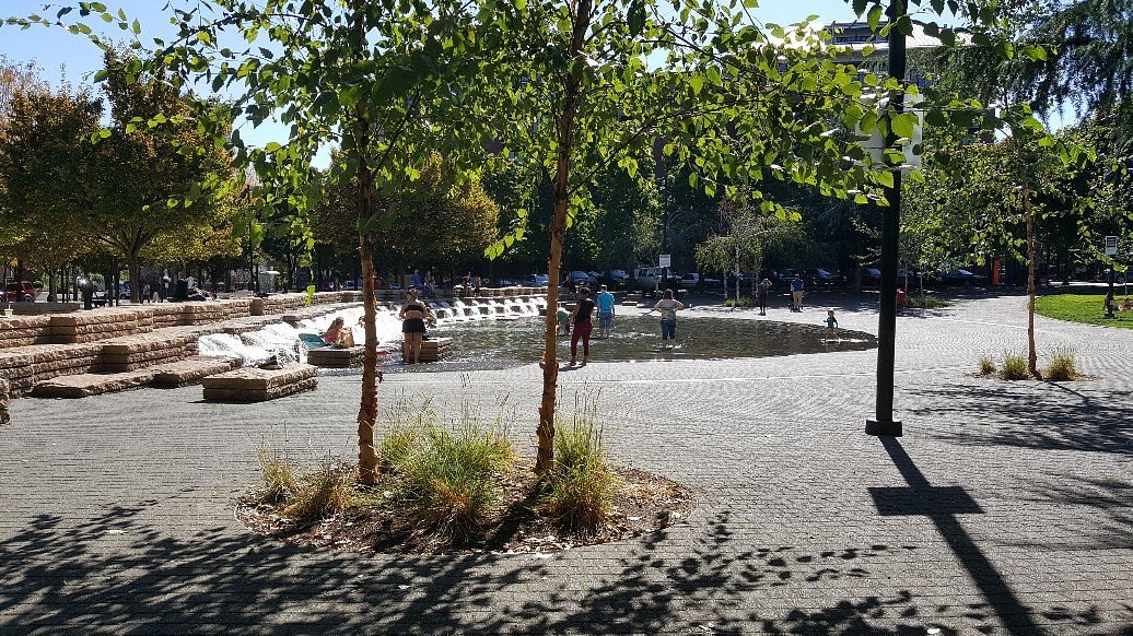 Jamison Square in Portland on a cloudy morning with people walking past the shallow fountain and brick buildings framing the park