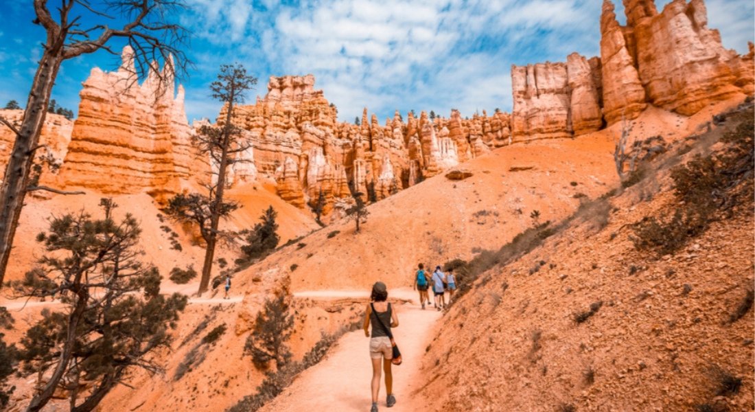 Morning hikers walking among hoodoos on the Queen's Garden Trail in Bryce Canyon with warm sunlight on the rocks