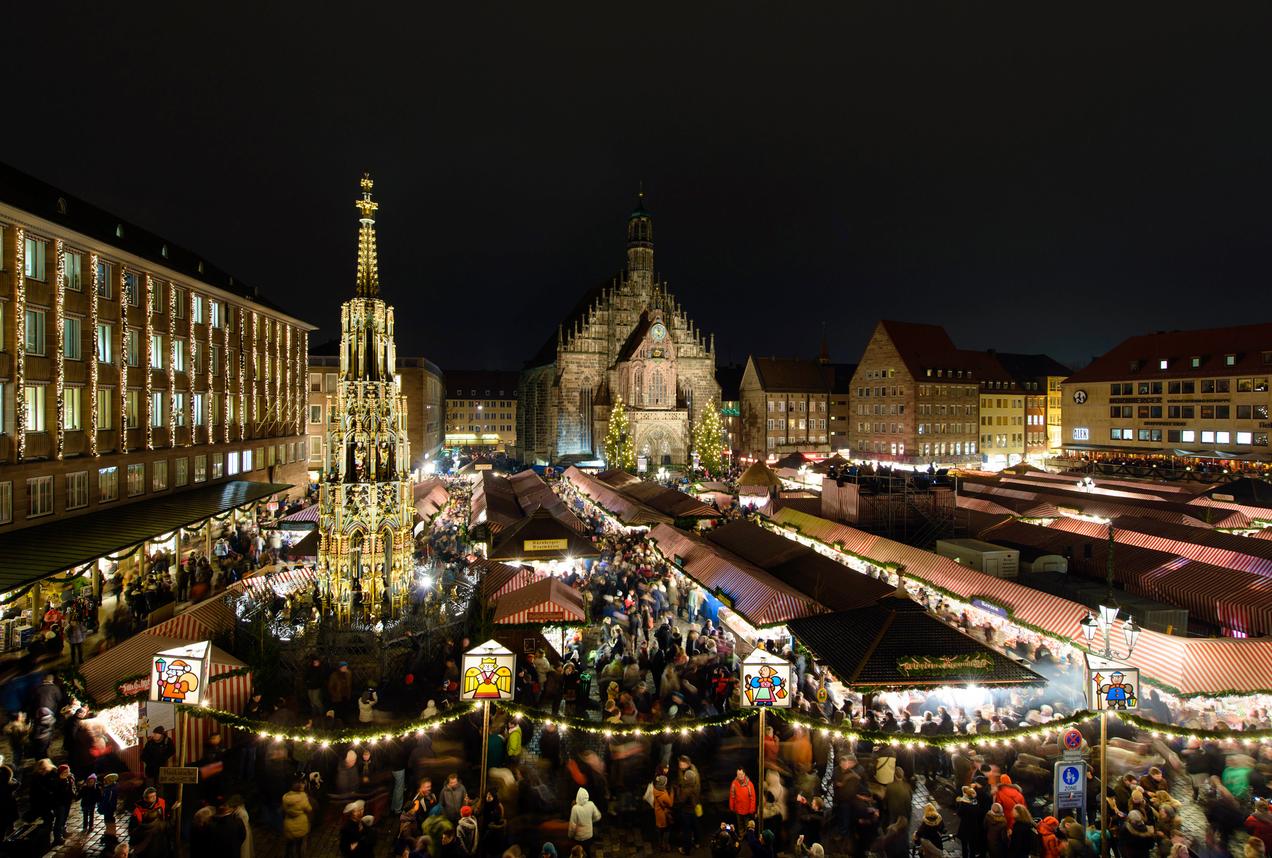 Nuremberg’s Hauptmarkt at night during the Christmas market, with rows of wooden stalls glowing under string lights and the illuminated facade of the Frauenkirche in the background, photorealistic travel photography