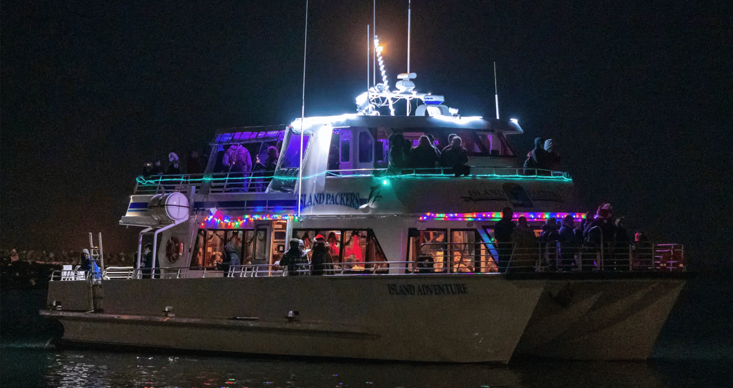 Small boats moored in Ventura Harbor at golden hour with warm light reflecting on calm water and harbor buildings in the background, realistic travel photography
