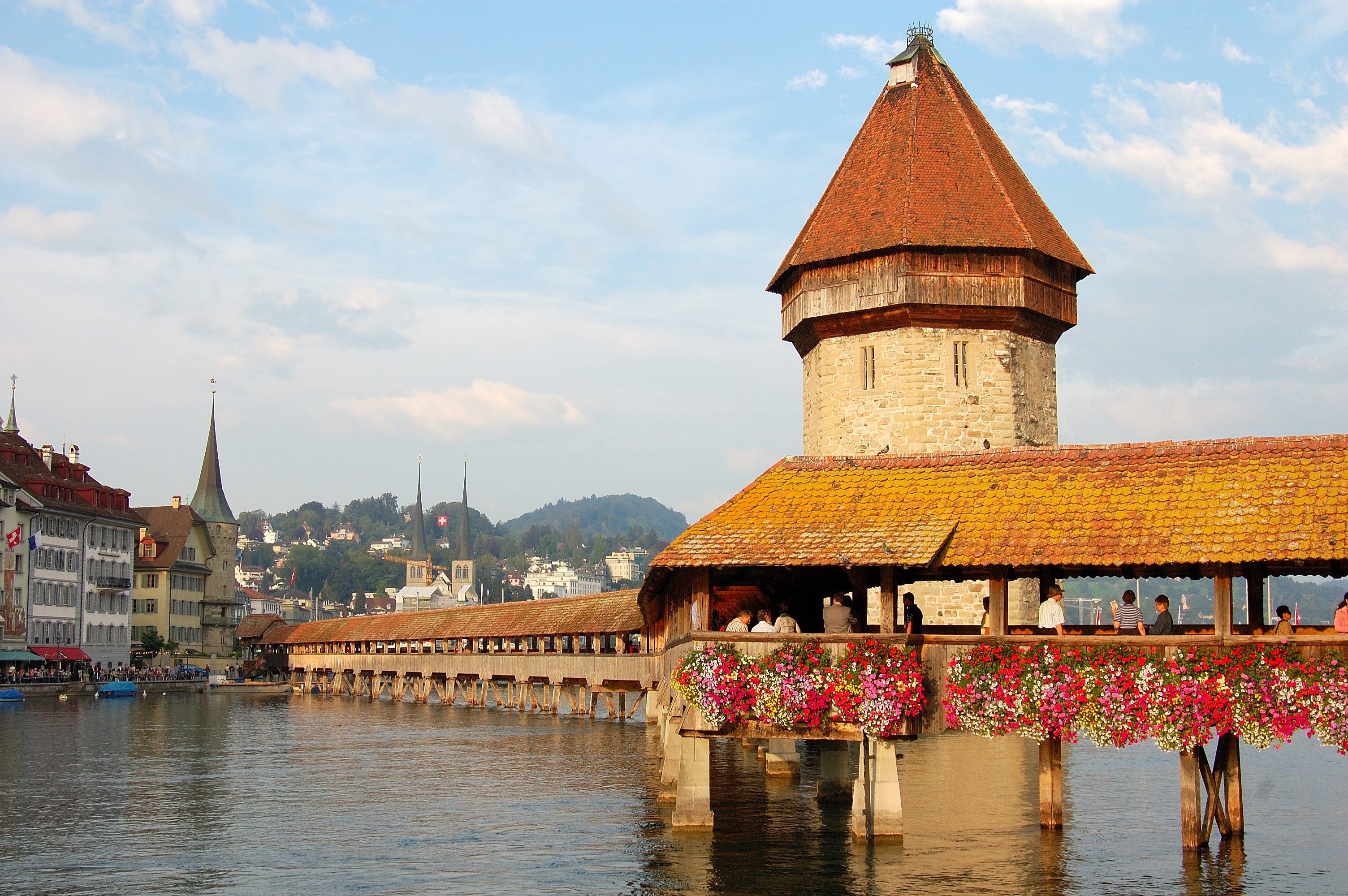 The Chapel Bridge in Lucerne stretching over the Reuss River at golden hour with historic buildings and soft reflections in the water, photorealistic travel photography