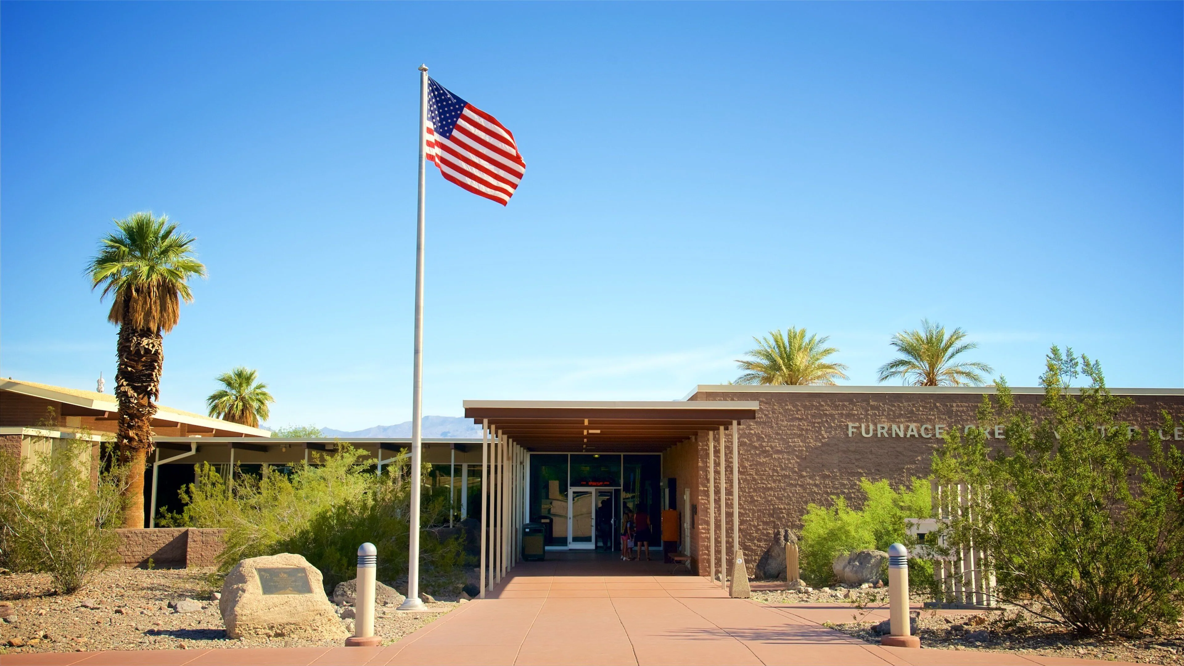 The Furnace Creek area in Death Valley with palm trees near park facilities under a clear blue sky, realistic travel photography