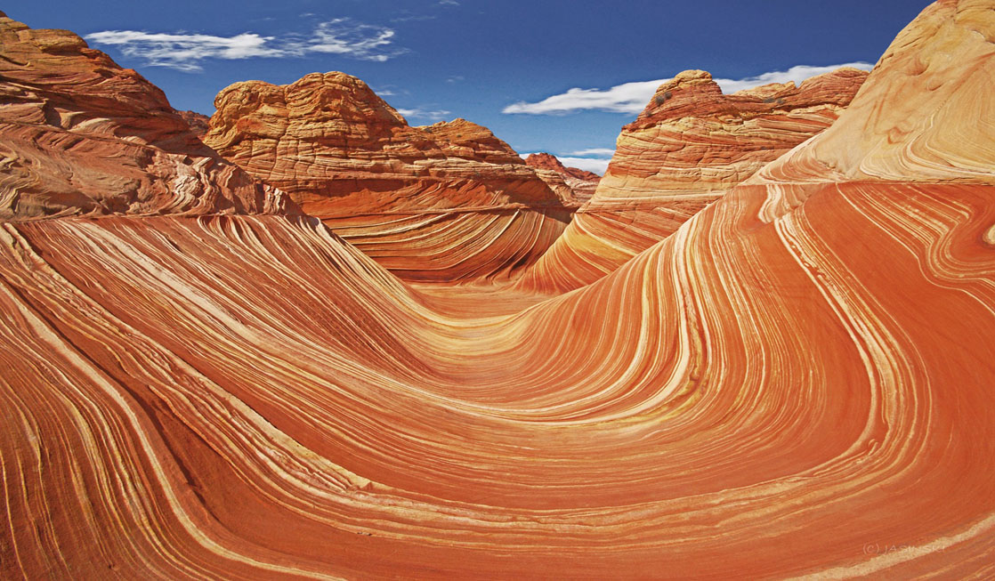 The Wave sandstone formation in Coyote Buttes North with smooth red and orange swirling stripes under clear desert light, photographed from trail level
