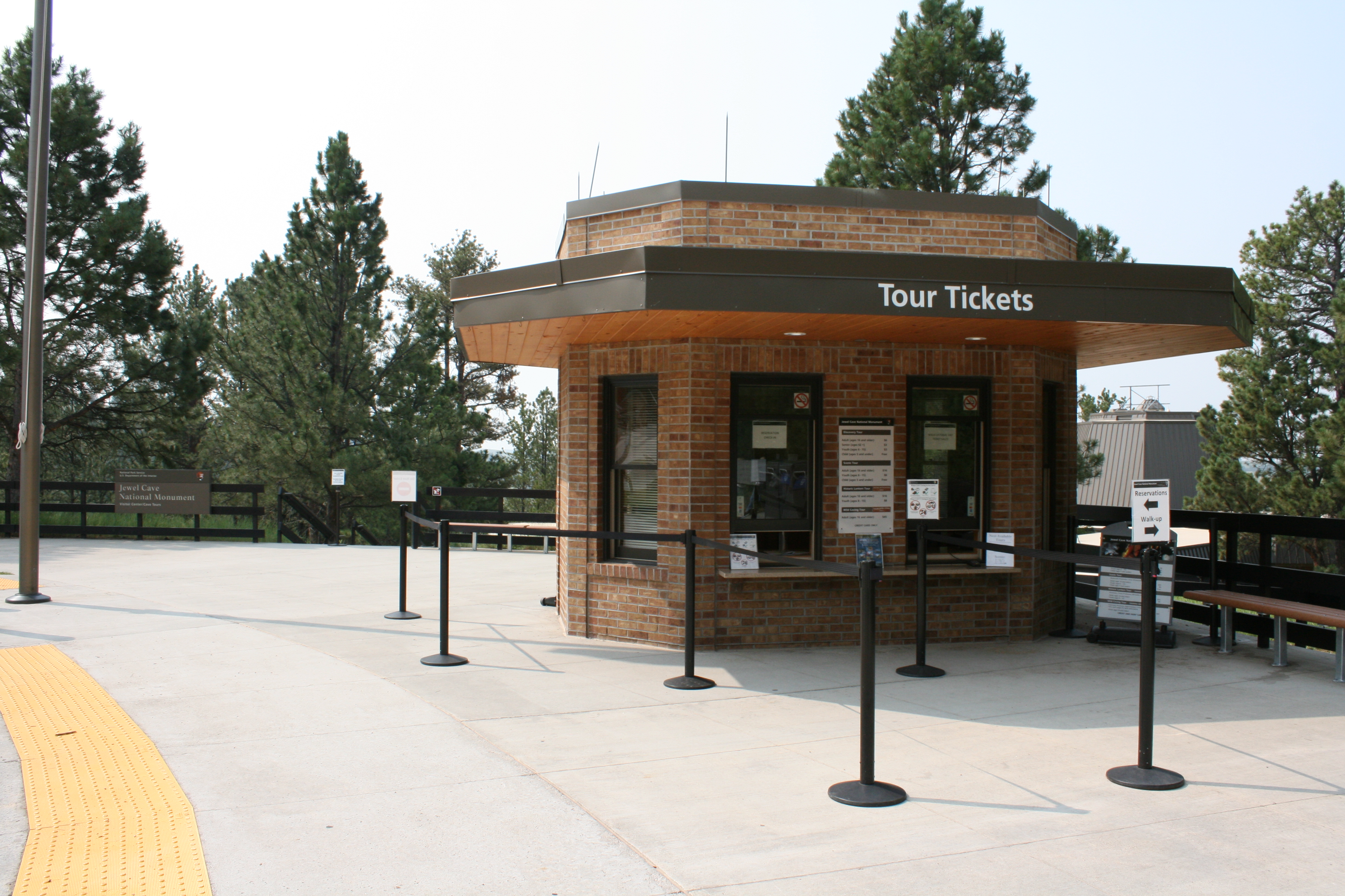 The rustic entrance area at Jewel Cave National Monument on a sunny day, with pine trees surrounding the visitor center and a few parked cars nearby