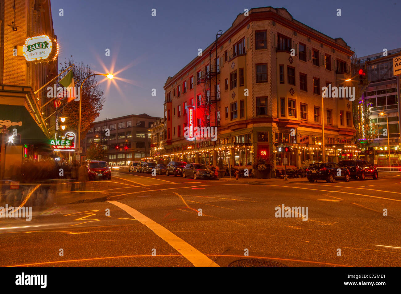 Tree-lined street in Portland's Pearl District at dusk with brick warehouses, modern storefronts, and pedestrians under soft streetlights