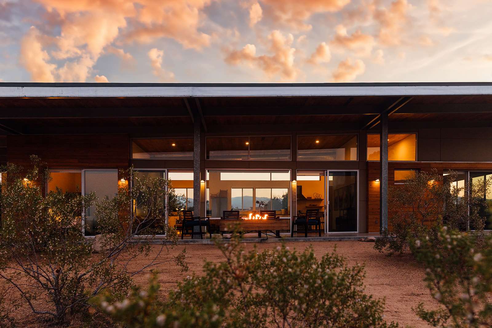 Two hikers resting in the shade of a desert canyon wall, water bottles and a small snack spread on a rock, harsh sunlight visible beyond the shaded area