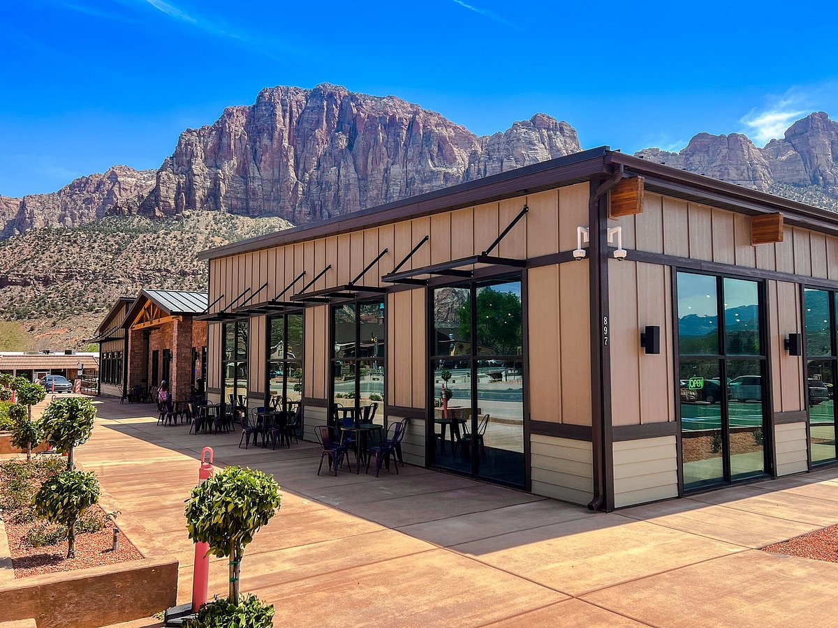 Two hikers resting on a coffee shop patio in Springdale, Utah with dusty hiking boots and iced coffees on a small table, warm late afternoon light, realistic photo