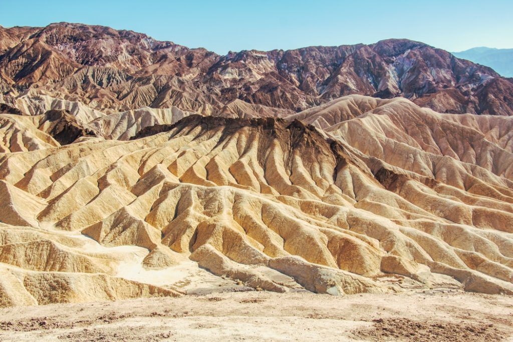 Two hikers walking through the narrow golden sandstone walls of Golden Canyon in Death Valley National Park during soft morning light, realistic travel photography