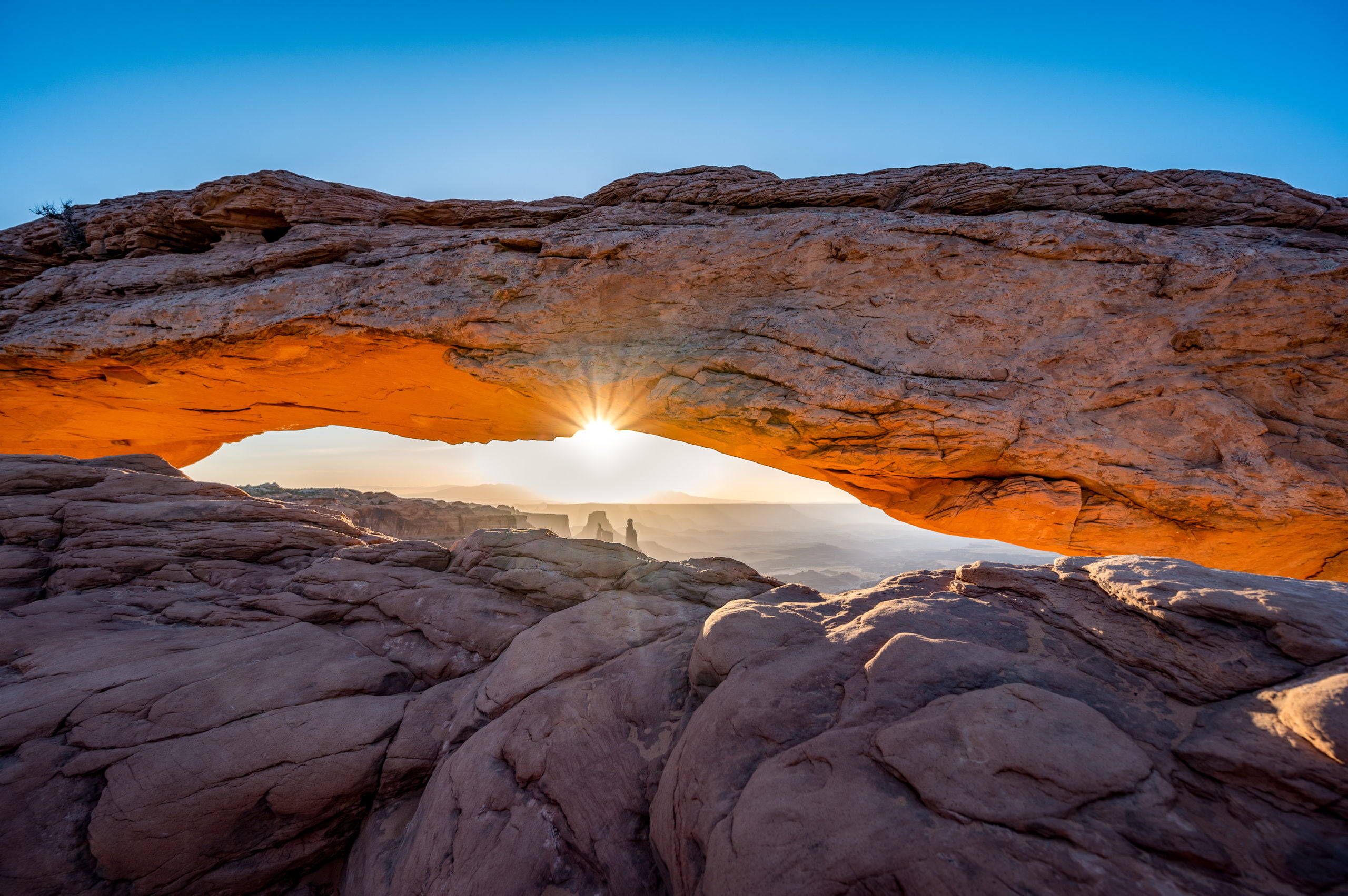 View through Mesa Arch at sunrise with glowing light under the arch and the canyon beyond