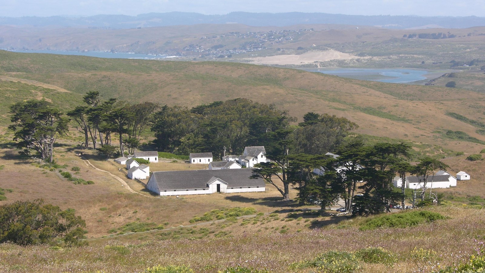 Weathered wooden ranch buildings at Pierce Point Ranch in Point Reyes with grassy hills and a pale coastal sky, documentary travel photograph